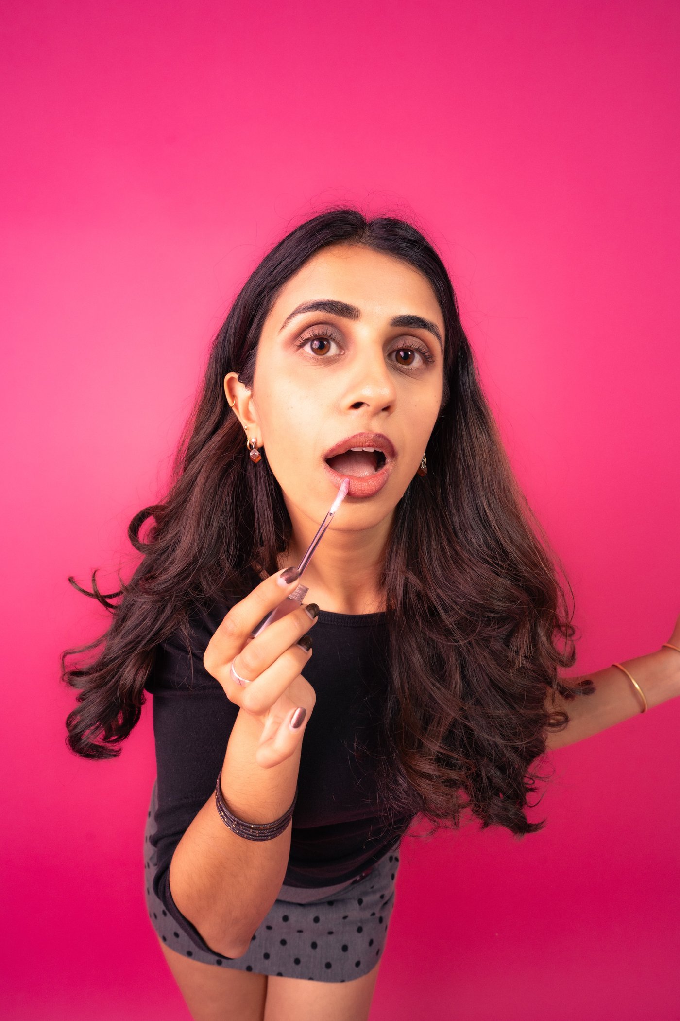 Close-up of Ashna applying lip gloss and looking up, playful expression.